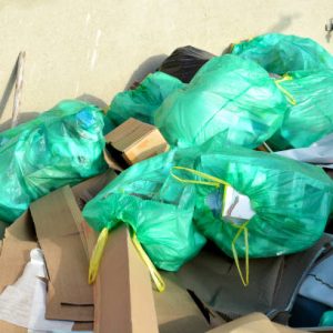 Green plastic bags with yellow trash ties are on top of a pile of torn cardboard boxes and other rubbish. Close-up.